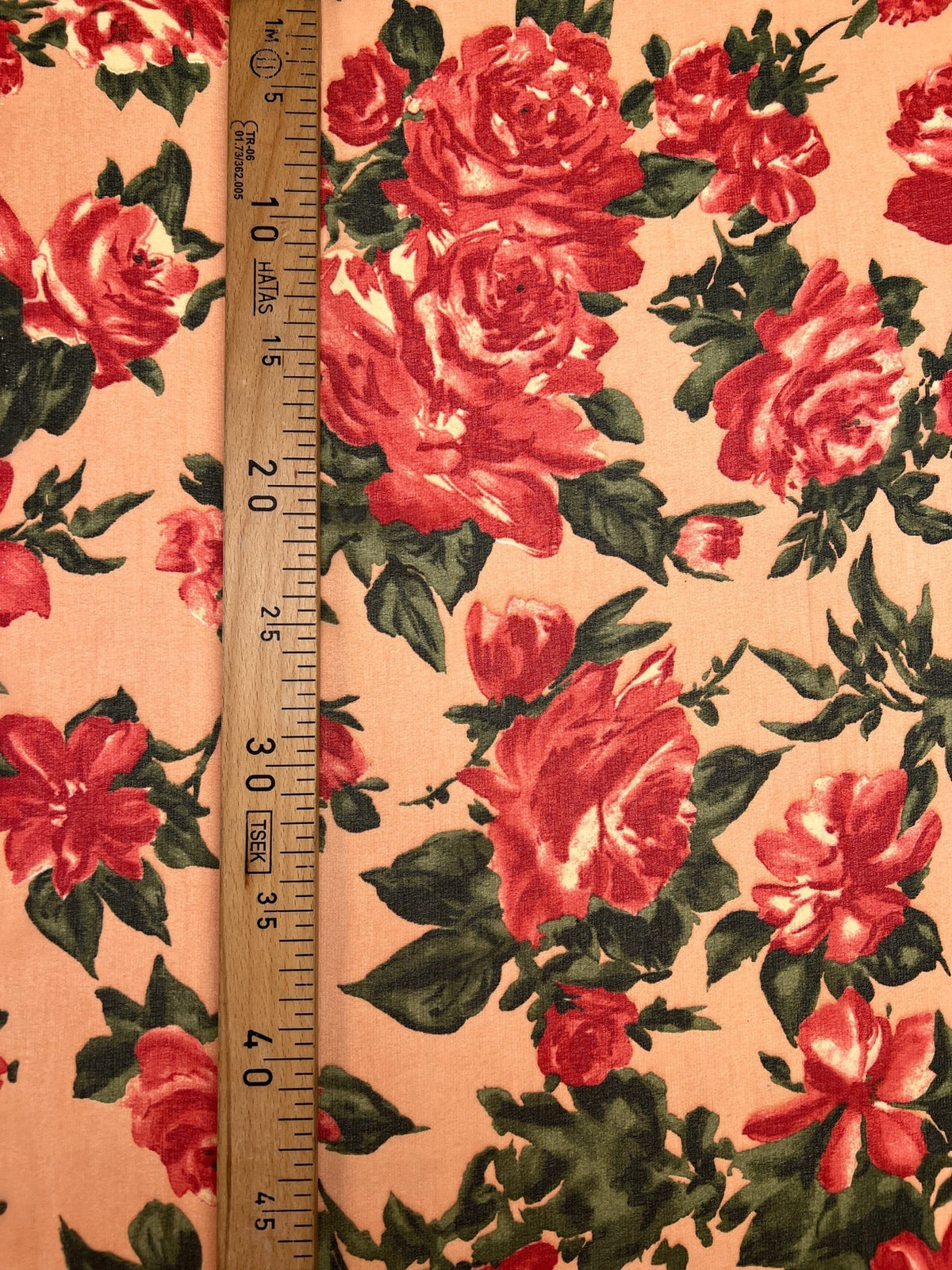 Image d’un tissu crêpe en polyamide à motif floral rouge sur fond beige – Italie – disponible en ligne chez Šarlotes audumi